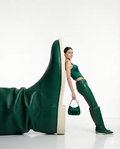 A Confident Woman Leaning Casually Against an Oversized Green Leather Boot Sculpture